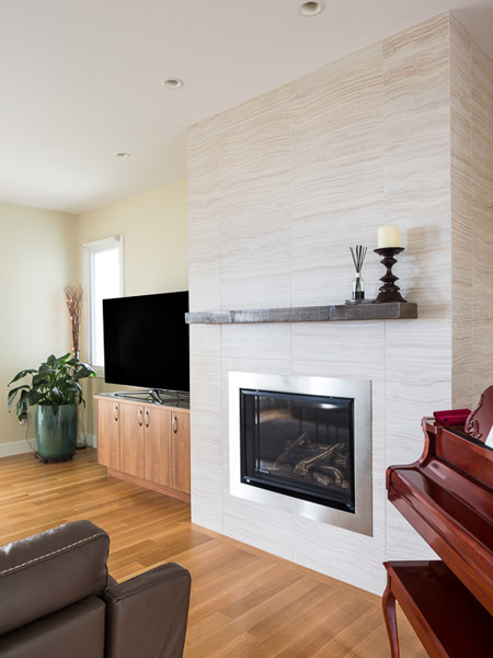The living room also features a gas fireplace with Statements Velvet II large-format tile and a reclaimed wood mantle, a rustic counterpoint to the clean lines of the fireplace and adjacent cabinets.