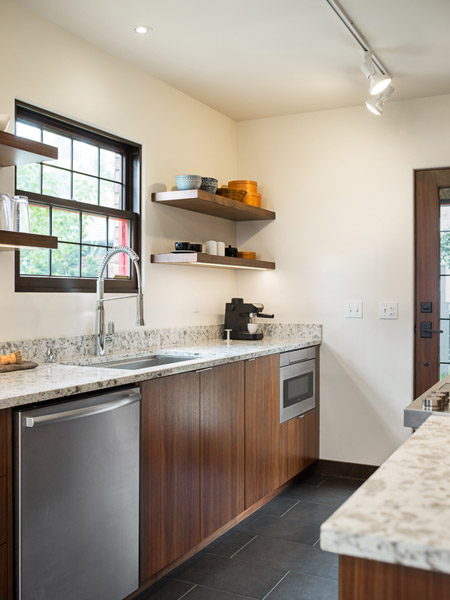 Quartered walnut custom cabinets bring rich wood tones to a kitchen that is otherwise finished with lighter colors and spare finishes, with shelving over the sink