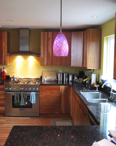 The renovated kitchen is in the same location as the old one, but features cherry cabinets, granite counters and blown-glass pendant lights over the eating area, remodel Seattle rambler
