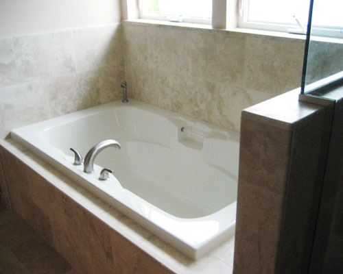 A drop-in tub surrounded by travertine tile is made for relaxation in this Seattle bath remodel