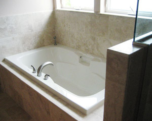 A drop-in tub surrounded by travertine tile is made for relaxation in this Seattle bath remodel