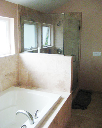 The shower directly to the side features a frameless glass enclosure and more travertine