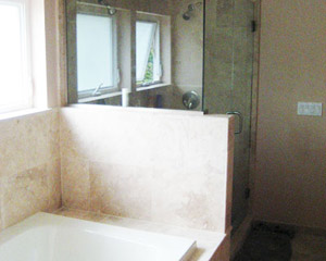 The shower directly to the side features a frameless glass enclosure and more travertine