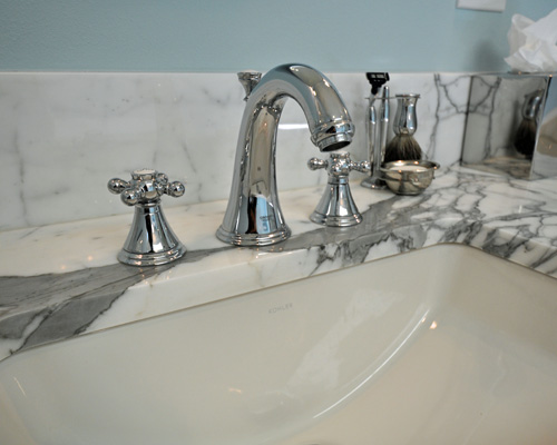 The 3cm calcutta gold marble counter and backsplash have rich veining, and the chrome fixtures shine on this traditional vanity top