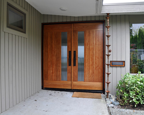 The new cherry doors with small glass lites are stunning, with rich grain and color.  Siding, the doorbell, and mail slot were all replaced and relocated a bit for a more deliberate presentation.  The old rectangular downspout is replaced with a modified copper rain chain assembly