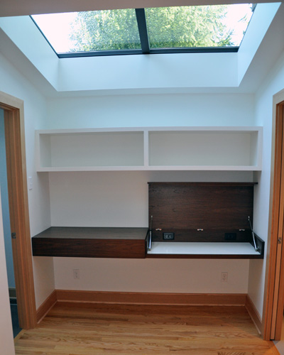 An expansive skylight illuminates the desk area, which features upper storage and a low-profile desk area made from dark Walnut