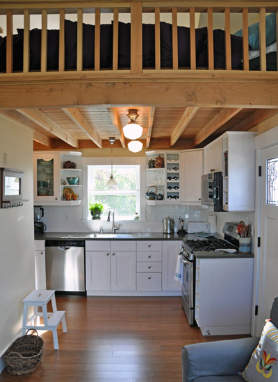 To the right, a functional kitchen takes up one corner of the floor space, with full range, sink and dishwasher.  The fridge is tucked out of sight in the corner. Countertops are Corian with Ikea cabinets
