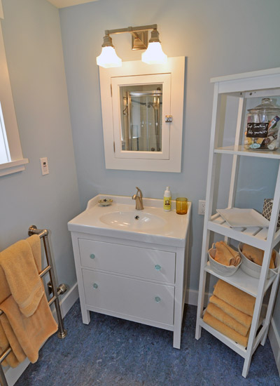 Through a second door, a petite vanity and sink fit along one wall, with toilet and neo-angle shower opposite.  Marmoleum flooring is used here, and a towel warmer ensures everything is cozy for guests