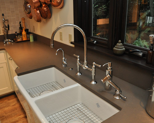 The kitchen is outfitted with a mix of styles that work well together:  the farm-style sink and traditional chrome fixtures blend with flashy copper pots and a honed quartz countertop