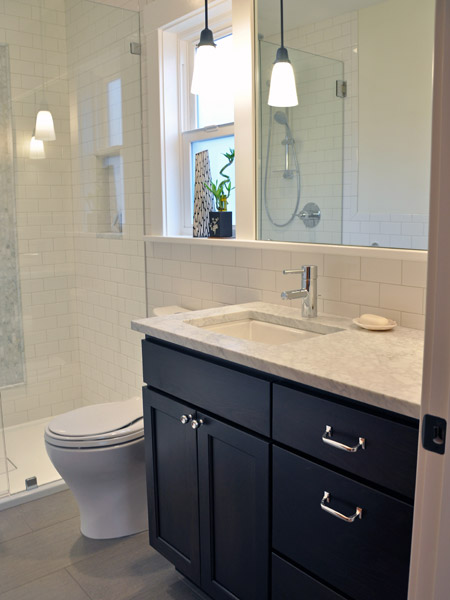 The vanity is in a dark-stained wood, and a matching linen cabinet is tucked across from it behind the door