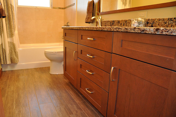 The finished bath benefits from a new window, with sloping sill at the tub.  The previous installation was problematic.  A deco line brightens the tile selection there, complimenting a new acrylic tub.  The porcelain tile floor - Cronin Natif Ginepro - simulates the look of wood, bringing in rich earth tones, tones mirroring the cherry cabinets