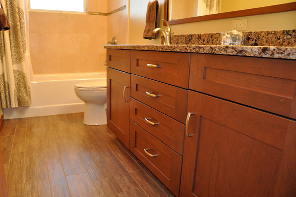 The finished bath benefits from a new window, with sloping sill at the tub.  The previous installation was problematic.  A deco line brightens the tile selection there, complimenting a new acrylic tub.  The porcelain tile floor - Cronin Natif Ginepro - simulates the look of wood, bringing in rich earth tones tones mirroring the cherry cabinets