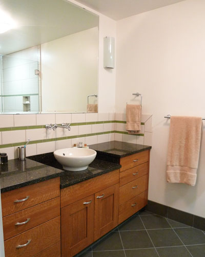 Across from the shower, an innovative design provides high counters on each side of the vessel sink.   Custom cabinets made from quarter sawn oak provide warm colors in this otherwise modern design