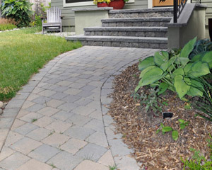 A concrete walk was removed to install a new curving paver pathway to the front door, widening to the length of the new front porch